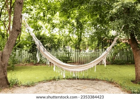 Comfortable Hammock hanging hanging on tree in summer garden. Cozy hygge place for weekend relax in yard. Hammock in boho style hanging on tree. Cozy exterior backyard. Concept of recreation outdoor. 