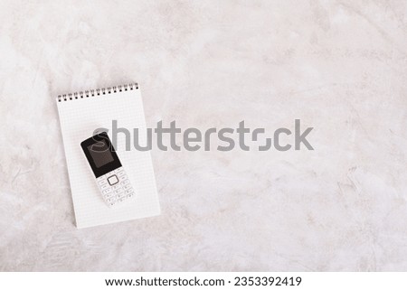 Old-fashioned feature telephone on a notepad on a gray background top view