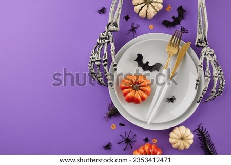 Creating a scary Halloween table. Top view flat lay of plates, cutlery, halloween decorations, spooky skeleton hands, orange pumpkins, confetti on purple background with banner area