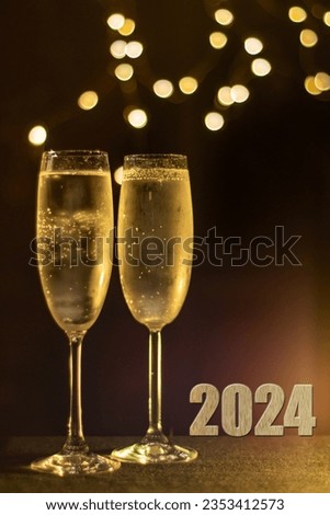 2024 image with two glasses of frosted Champaign against a soft party light bokeh background. Selective focus on the right hand frosted glass. 2024 new year concept. 