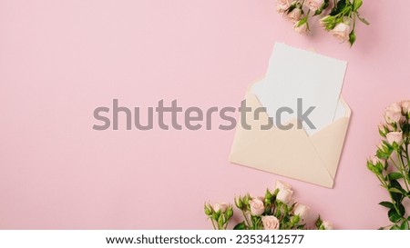 Blank paper card inside envelope with roses on pink background. Flat lay, top view, copy space.