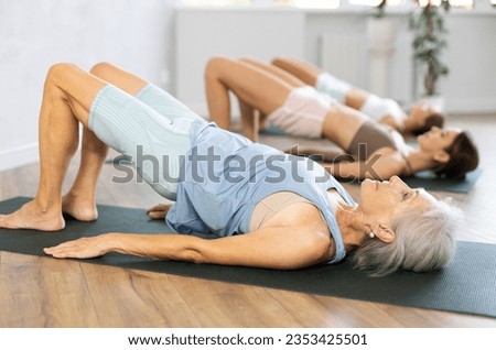 Women three generations doing glute bridge exercise, dvi pada pithasana pose, working out in yoga studio Royalty-Free Stock Photo #2353425501