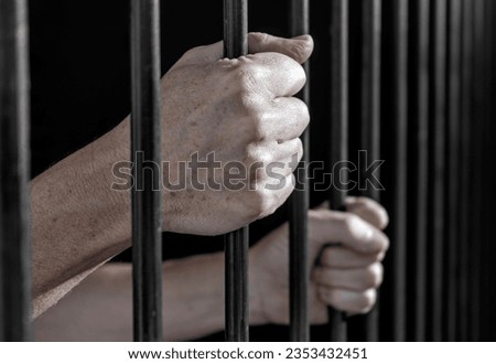 Prisoner's hands gripping the bars of a cell in jail or prison serving sentence. Royalty-Free Stock Photo #2353432451