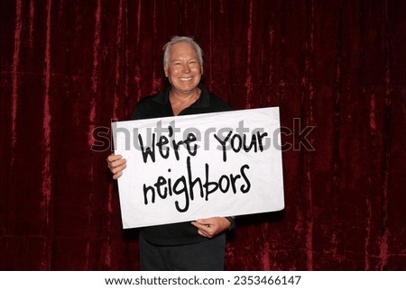 Photo Booth. Large Sign. A man smiles and laughs as he holds a large sign that reads We're your neighbors while in a Photo Booth. Neighbors love a Photo Booth for all parties and events. Photo Booth.  Royalty-Free Stock Photo #2353466147