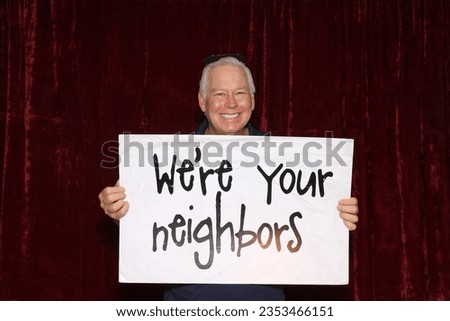 Photo Booth. Large Sign. A man smiles and laughs as he holds a large sign that reads We're your neighbors while in a Photo Booth. Neighbors love a Photo Booth for all parties and events. Photo Booth. 