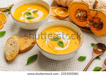 Plate of pumpkin carrot soup served with herbs, cream and crusty bread.