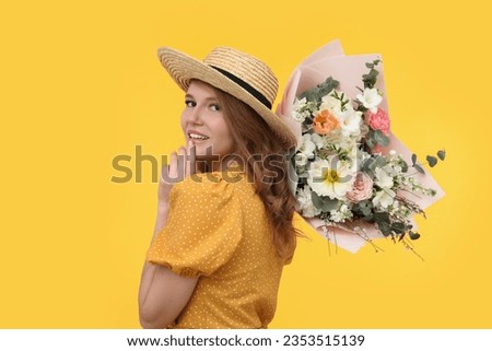 Beautiful woman in straw hat with bouquet of flowers on yellow background