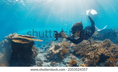 Underwater photographer takes pictures of the healthy coral reef. Freediver with camera swims over the reef. Nusa Penida, Bali, Indonesia