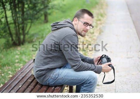 Young Man Sitting on a Bench in Park with Photo Camera