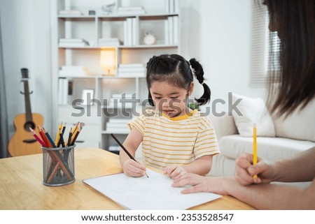 Cute little child painting with colorful paints. Asian girl and mother using crayon drawing color. Daughter and mom doing homework coloring cartoon characters. Baby artist activity lifestyle concept.