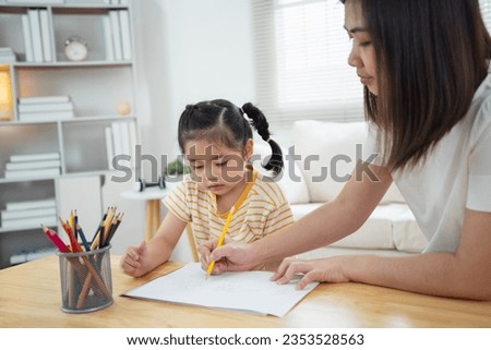 Cute little child painting with colorful paints. Asian girl and mother using crayon drawing color. Daughter and mom doing homework coloring cartoon characters. Baby artist activity lifestyle concept.