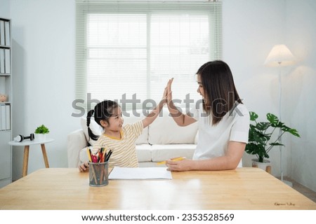 Cute little child and mom hands making give me five while painting with colorful paints. Asian girl and mother using crayon drawing color. Daughter and mom doing homework coloring cartoon characters.