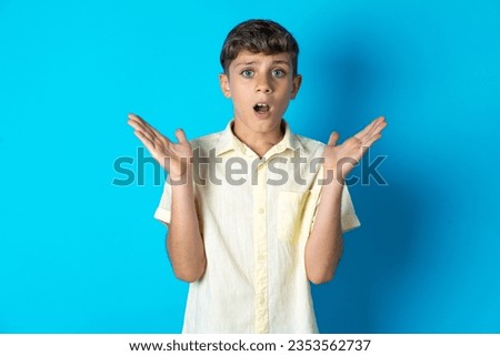 Surprised terrified Beautiful kid boy wearing casual shirt Gestures with uncertainty, stares at camera, puzzled as doesn't know answer on tricky question, People, body language, emotions concept