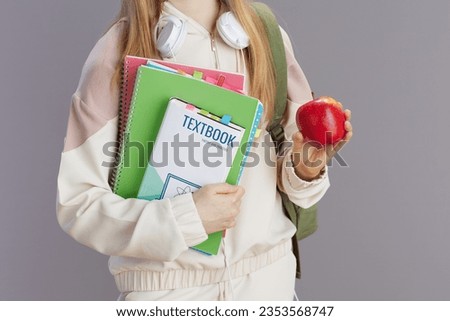 Closeup on teenager girl in beige tracksuit with apple, backpack, workbooks, headphones and textbook isolated on grey background. Royalty-Free Stock Photo #2353568747