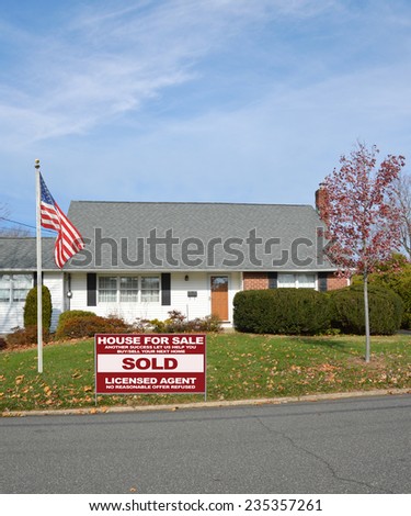 American flag pole Real Estate sold (another success let us help you buy sell your next home) sign suburban bungalow style home autumn season residential neighborhood blue sky clouds USA