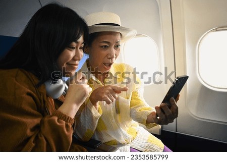 Happy retried woman and daughter sitting in passenger airplane and taking picture, waiting for airplane landing