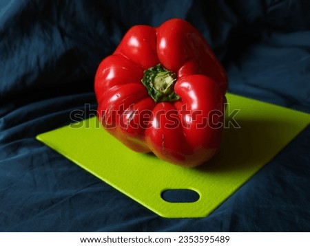 A sweet red pepper, flecked with signs of decay, lays gracefully on a green plastic tray. The bright red shade of the pepper harmoniously contrasts with the greens of the tray.