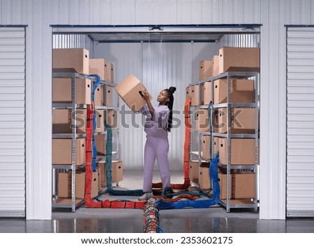 Woman standing in garage with shelving units, moving cardboard storage boxes. Ethernet cables run in between shelves. Metaphor for concepts of cloud computing, cloud storage, data center, server park 
