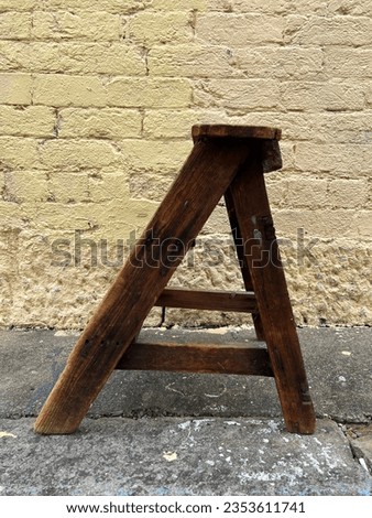 Yellow weathered urban warehouse brick wall with vintage antique wooden step ladder in front Royalty-Free Stock Photo #2353611741