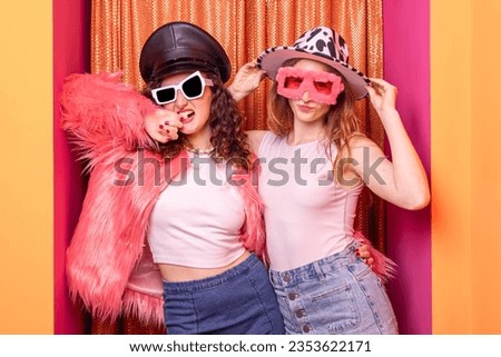 Attractive couple of casual caucasian women posing having fun standing with yellow - orange background hugging and making face.