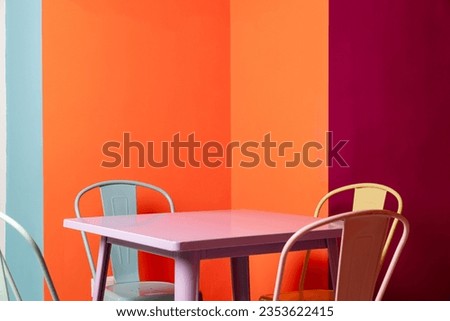 pink fast food restaurant table with yellow, blue colored chairs and an orange, yellow, purple and blue background