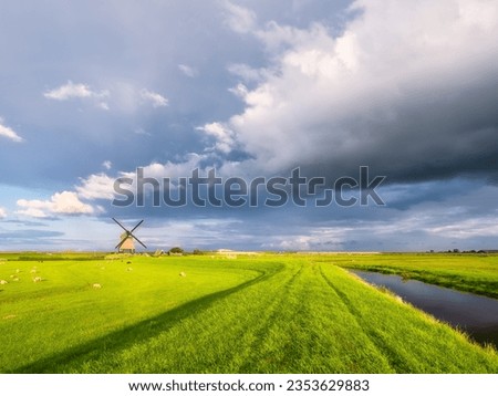 Minimalistic landscape with a windmill. A huge cloud before a storm. Field and pasture for animals. Agricultural fields and pastures. Summer landscape in the Netherlands.