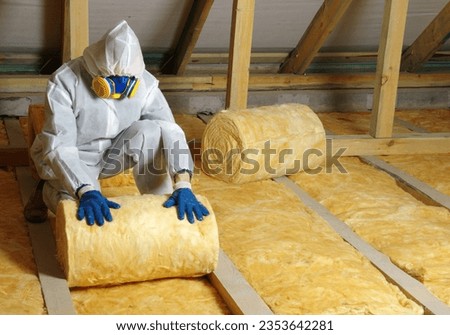 Construction worker thermally insulating house attic with glass wool  Royalty-Free Stock Photo #2353642281
