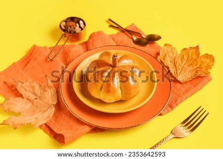 Plates with tasty pumpkin shaped bun on yellow background
