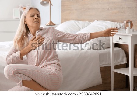 Mature woman with heart attack taking pill in bedroom Royalty-Free Stock Photo #2353649891