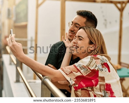 Portrait of a young happy couple having fun taking a selfie with camera on smartphone outdoors. Girlfriend and boyfriend bonding, love concept during summer.
