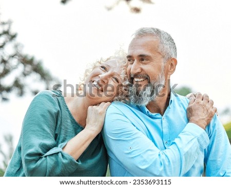 Happy active mid middle aged adult mature couple having fun talking and hugging in park outdoors