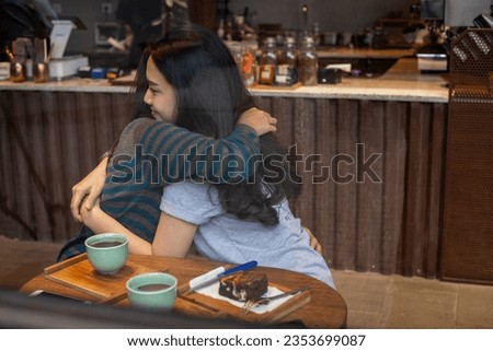 Two women hugging each other behind a window in a coffee shop