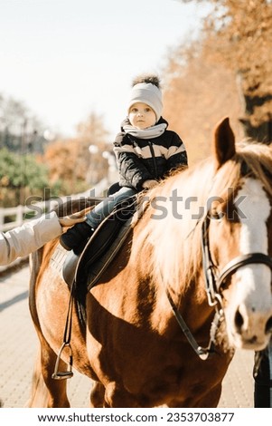 Child on a horseback closeup. Kid riding a horse. Family having fun spring vacation on horse ranch. Children ride horses. Little boy in saddle on horse. Animal love. Soft focus on face.