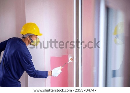 side view Asian painter male worker paints a wall with a paint roller Repainting the walls inside the house white with a paint roller. Home interior ideas. Royalty-Free Stock Photo #2353704747