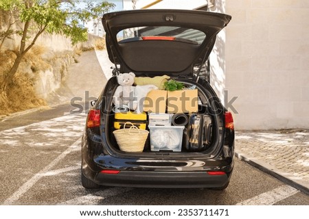 Moving boxes and suitcases, various belongings, plants in open trunk of black car outdoor on the street next to building, no people, copy space. Relocation, moving, real estate, new beginning concept Royalty-Free Stock Photo #2353711471