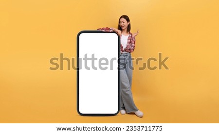 Great mobile af. Happy asian lady leaning on huge giant cellphone with blank screen and shouting wow, female standing isolated over yellow background, panorama, banner