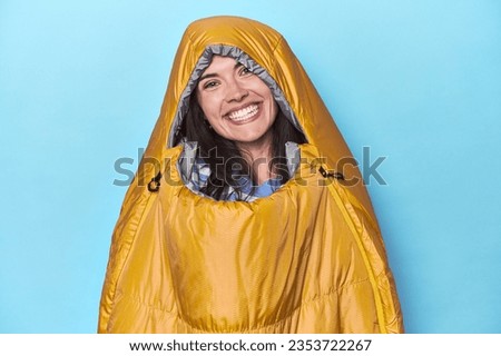 Woman in sleeping bag on blue background happy, smiling and cheerful.