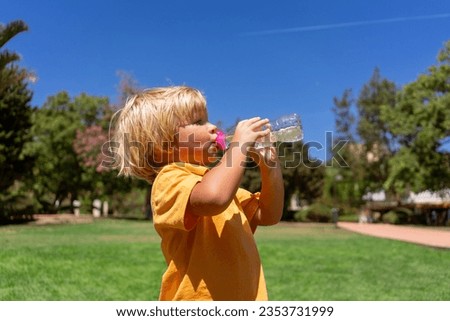 little boy drinks water in the park in summer. thirst