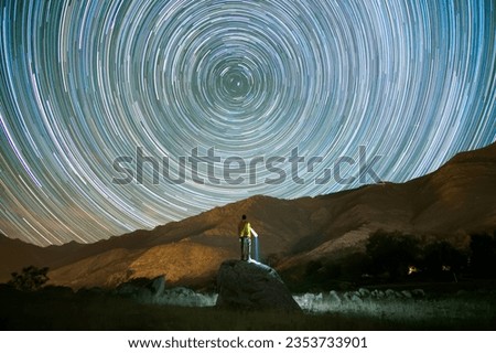 rear view of man climbed on a rock looking at star trails at night