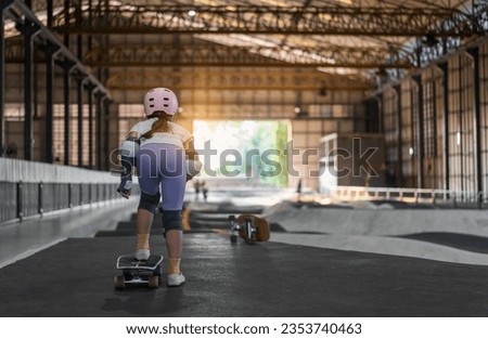 asian child skater or kid girl start riding surf skate at indoor pump track or fun playing skateboard in skate park by extreme sports surfing to wearing helmet elbow pads wrist knee guard body safety Royalty-Free Stock Photo #2353740463