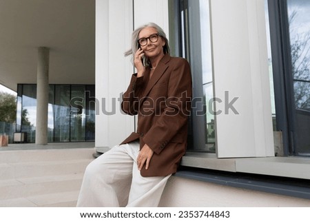 confident mature old lady with gray hair in glasses wearing a brown jacket is waiting for a call from a business partner Royalty-Free Stock Photo #2353744843