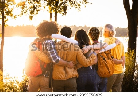 Experience the beauty of connection and nature's splendor in this heartwarming image. Young people with backpacks stand close, sharing an embrace while admiring the breathtaking sunset view over the Royalty-Free Stock Photo #2353750429