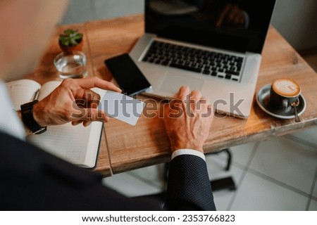 High angle shot of a busy man sitting at the coffee shop and holding a credit card in his hand while using his laptop with the other.Paying his purchase remotely while using online banking.Copy space.