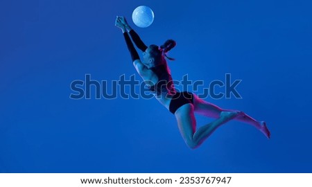 Professional female athlete, young woman playing volleyball, in motion hitting ball against blue studio background in neon light. Concept of professional sport, competition, health, hobby, action, ad