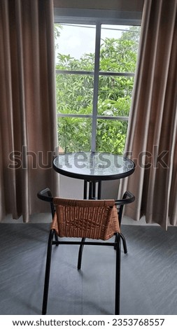 Picture by the window. There are chairs and a table by the window. and dark curtains