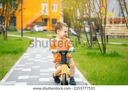 A cute happy toddler boy of two or three years old rides a bicycle or balance bike in a residential complex on a sunny summer day. Active kid playing outside.