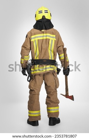 Strong firefighter in helmet and uniform holding fire axe in studio. Back view of unrecognizable male fireman in full gear holding hatchet tool for work ,on gray background. Concept of fire equipment. Royalty-Free Stock Photo #2353781807