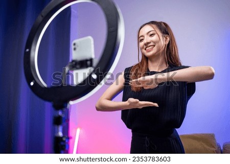 Young trendy influencer asian woman dancing on mobile phone at home in living room with neon light. Creator vlogger talent dancing enjoy hobby content recording show video sharing on social media. Royalty-Free Stock Photo #2353783603
