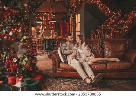 Portrait of young lovely couple hugging indoor eve 25 December. Lovers laughing hugs kisses waiting xmas at home. Celebrating new year garlands lights noel in elegant knitwear outfit tenderness Royalty-Free Stock Photo #2353788855