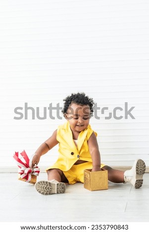 Portrait images, A 2-year-old Nigerian baby girl with beautiful curly hair, smiling and happy while reaching out into the gift box, on white background. to African baby and gift box concept.